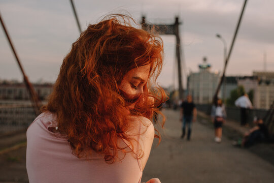 Back view of woman with red hair walking on bridge in city