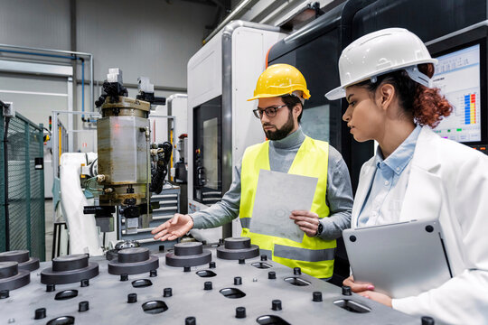 Engineer with colleague examining machine parts in factory