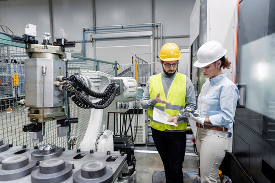 Young engineer explaining colleague with machine part in factory