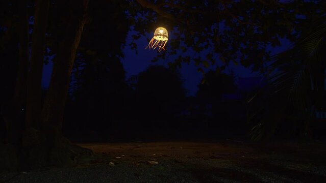 Bright lantern hanging on the tree at night in windy weather, Thailand
