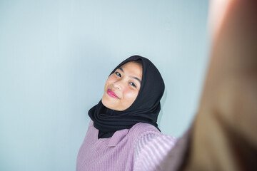 Happy young muslim woman take self portrait with handphone at home. Happy arab woman in hijab with mobile phone making selfie. Portrait of smiling girl, posing.