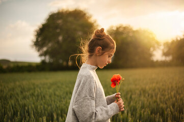 Girl holding poppy flower in green field at sunset