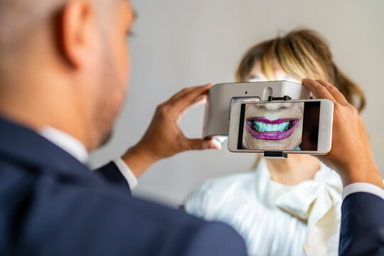 Businessman photographing colleague's smile through mobile phone using magnification equipment