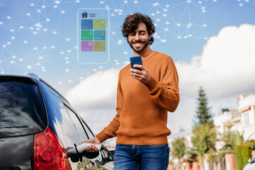 Happy young man using smart phone charging electric car