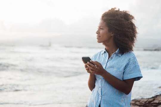 Thoughtful woman with mobile phone standing in front of sea
