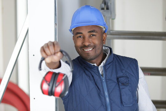 male worker holding forwards a pair of ear defenders