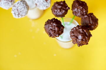 Delicious homemade popcake coconut and dark chocolate cake pops on a yellow background, festival desserts, tasty food