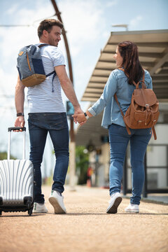 Rear View Of Stylish Travelers With Backpacks At Train Station