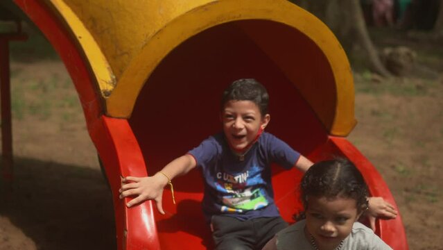 three happy children coming down a tube slide in a park (close up of exit)