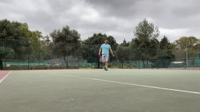 man in white walking on tennis court with racket in hand. Male tennis on grass. Club tennis concept.