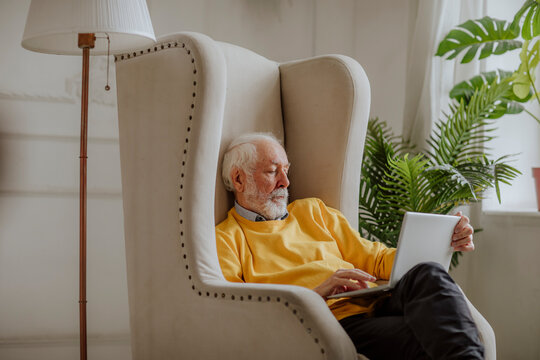Senior freelancer using laptop on armchair at home