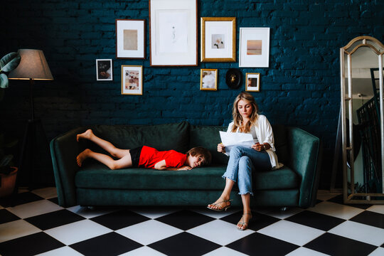 Woman with documents sitting by boy lying on sofa at studio