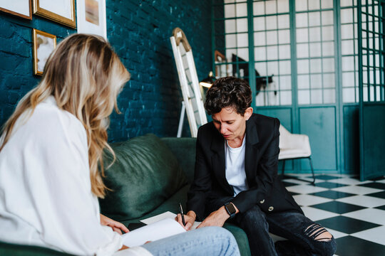Producer signing document by actress sitting on sofa at film set