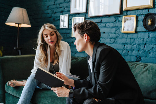 Producer holding book talking to actress sitting on sofa at film set