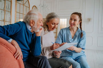 Senior woman signing document with man and caregiver at home