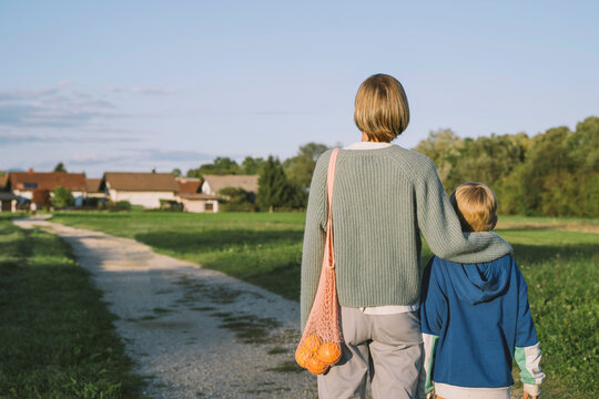 Woman with arm around son standing on footpath
