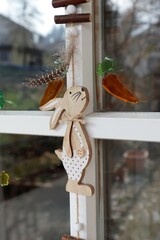 Easter decorations on the door. The bunny wants a carrot. The front door is decorated with a garland with a wooden bunny and chicken feathers. Slime carrots and flowers on the glass.