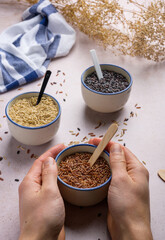 Hand holding a bowl of red rice. There are several types of rice