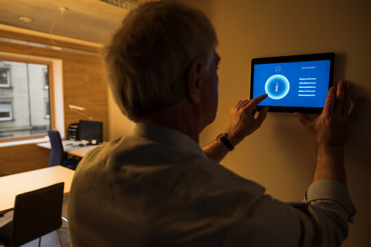 Businessman adjusting temperature through tablet PC mounted on wall at office