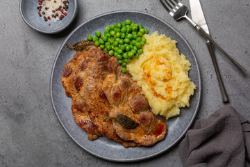 Top view of fried pork steaks with spices and sage, mashed potato and boiled green peas.