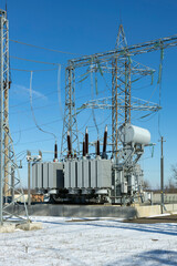 A power transformer in a high-voltage electrical substation outdoors in winter.