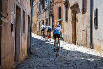 Istria, Croatia - Apr 19, 2018: Cyclists riding down the narrow cobblestone street in the ancient town of Motovun