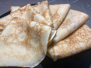 On a black plate neatly laid pancakes folded into envelopes. The pancakes are fresh and delicious. Pancakes close-up.