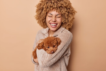 Portrait of cheerful curly haired young woman laughs happily expresses positive emotions has fun...