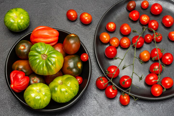 Naklejka na ściany i meble Red cherry tomatoes on a twig, green tomatoes in black plates.