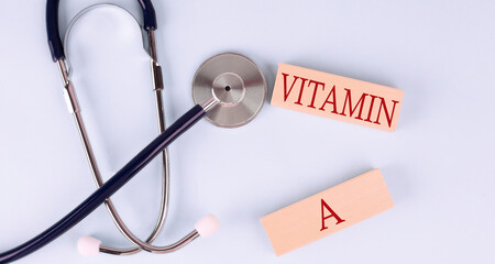 On a blue background, a stethoscope and wooden block with the word VITAMIN A .Medical concept