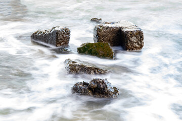 A long exposure photo of stones in the sea near the shore with beautifully blurred water and clear rocks. The concept of calmness and stability in any situation.