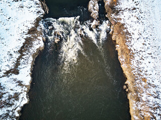 Waterfall on winter creek. Snow on frozen riverbanks. Top Aerial View Of River Cascade. Stream water flowing between rocks - 578271797