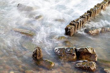 Fototapeta na wymiar Beautiful long exposure photo of wooden coastal structures on the seashore. The blurred water creates a calming and serene atmosphere, while the wooden elements add texture and depth to the image.