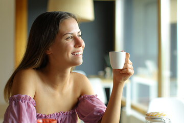 Happy teen holding coffee cup looking through a window at home