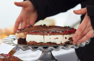 Vendor at a market confectionery stall arranging a cheesecake on a stand, spring cold day.