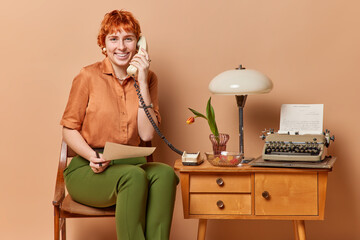 Positive red head retro businesswoman works in own cabinet from home holds paper document uses...