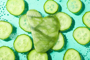 Slices of cucumber with gua sha in water on mint background