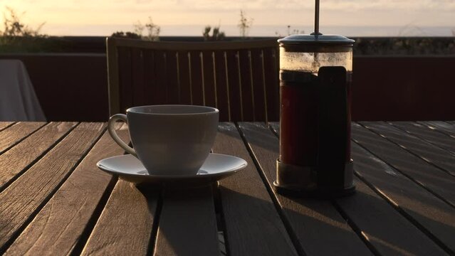 Caf&eacute; reci&eacute;n hecho en cafetera de &eacute;mbolo con bonita luz de amanecer y m&oacute;vil y gafas de lectura que son recogidas por la mano de un hombre