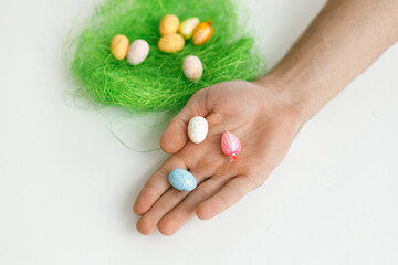 Easter toys. Easter toys with green leaves in the hands of a man. White background. Chicken eggs, twigs with green leaves on the hay. Easter holiday concept background.