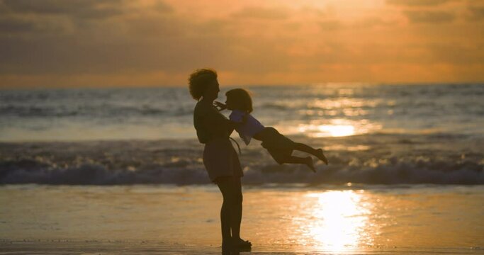 Mother swinging little girl around. Happy family on beach holding hands at sunset on vacation. Woman and her daughter spun around standing on wet sand near ocean water. Fun weekend. Slow motion. 