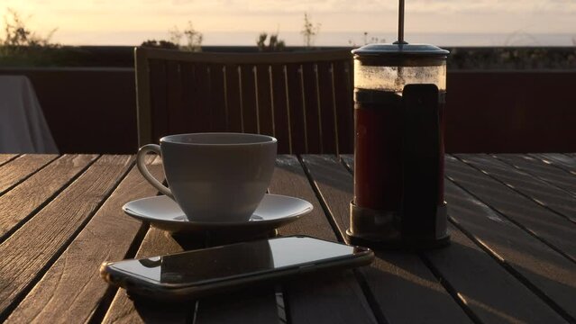 Caf&eacute; reci&eacute;n hecho en cafetera de &eacute;mbolo con bonita luz de amanecer y m&oacute;vil y gafas de lectura entran en el plano.