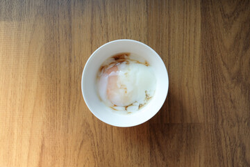 Soft boiled egg or Japanese onsen egg and shoyu soy sauce in the white bowl on wooden background.