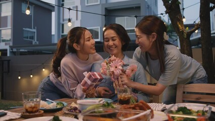 Mother's day two young child cuddle hug give flower gift box to mature mum. Love kiss mom asia people middle aged adult at home cozy dining table night dinner party happy smile enjoy relax warm time.
