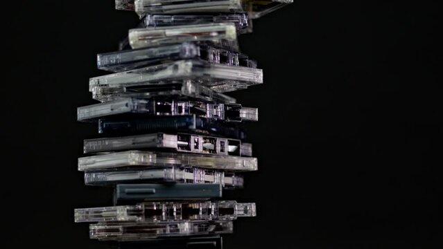 A stack of audio cassettes spins on a black background and mirror surface. Golden nineties.