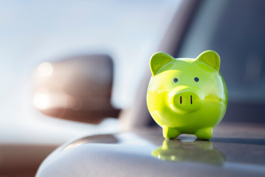 Green piggy bank money box on top of car hood, new vehicle purchase, insurance or driving and motoring cost