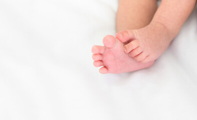 Tiny foot of newborn baby on white blanket at home
