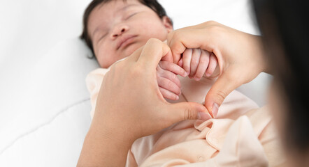 Mother holding hands of her newborn baby on white bedding