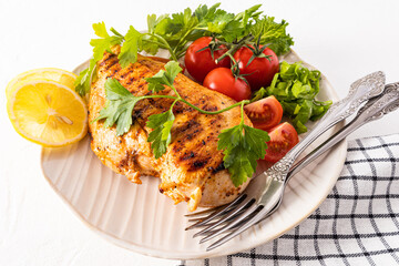 large textured ceramic plate with grilled chicken fillet with fresh vegetables. lemon wedges to improve the taste. white background.