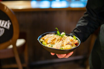 Men's waiter hands hold a Caesar salad with croutons, cheese, eggs, tomatoes and grilled chicken in pub