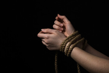 Women's hands tied with a rope on a black background.
